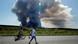 Personas pasan por una ruta, y en el horizonte se ve un iIncendio en el centro logístico de Wildberries tras un ataque con drones ucranianos. (18.07.2026).