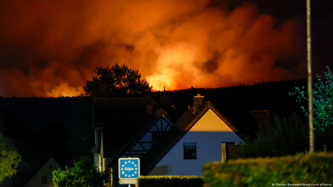 Imagen tomada desde Monschau en la que se ve el cartel de la frontera con Bélgica en primer plano y, al fondo, tras una elevación, el humo iluminado por las llamas a escasa distancia. Imagen tomada desde Monschau en la que se ve el cartel de la frontera con Bélgica en primer plano y, al fondo, tras una elevación, el humo iluminado por las llamas a escasa distancia.