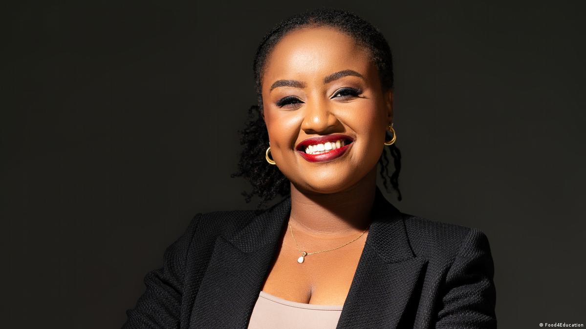 Portrait of Wawira Njiru, a smiling young woman wearing a black suit and beige top, in front of a black background.