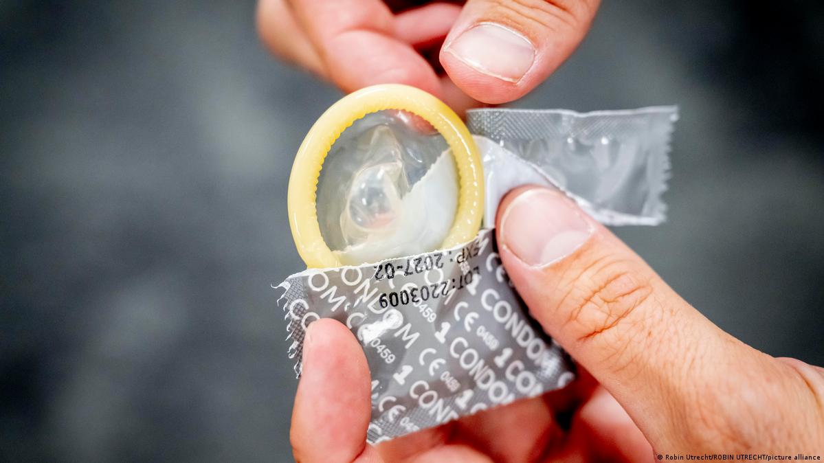 A person taking a condom from its wrapper. Clearly visible in the shot on the packaging are the CE markings used in Europe to show that it conforms with the consumer standards of the European Economic