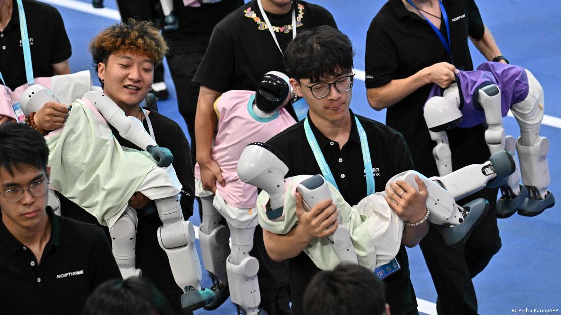 Pekin'deki Dünya İnsansı Robot Oyunları'nın ardından çalışanlar, insan biçimindeki robotları kucaklarında taşıyarak alandan çıkarıyor.