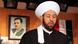 Ahmad Hassoun in a white head dressing with a blurred picture of Bashar Assad behind him Ahmad Hassoun in a white head dressing with a blurred picture of Bashar Assad behind him