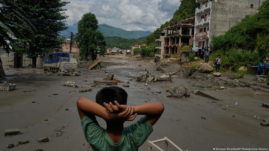 Nepal'in Nuwakot bölgesinde bir çocuk, selin ardından çamur, moloz ve hasarlı yapıların bulunduğu caddeye sırtı dönük şekilde bakıyor.