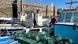 Image 2: Two eel fishermen stand on their boats beside stacked eel traps in a Spanish harbor