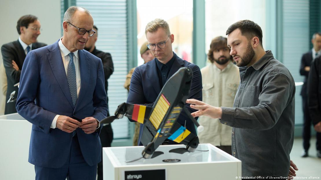 Германија Берлин 2026 | Канцлеларот Фридрих Мерц разгледува модел на дрон кој му го покажува маж со брада 
