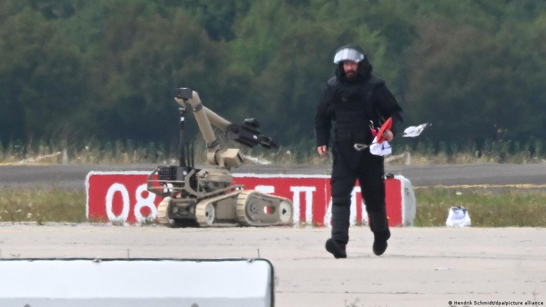 A bomb disposal technician operates alongside a robot near a Ukrainian aircraft at Leipzig/Halle Airport while defusing a drone fitted with an explosive device