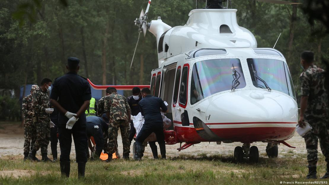 Ormanlık alanda, yerde duran beyaz bir helikoptere ceset taşıyan görevliler ve askerler Ormanlık alanda, yerde duran beyaz bir helikoptere ceset taşıyan görevliler ve askerler