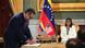 El presidente de Chevron, Mariano Vela, firma un papel en un marco institucional. Dos banderas de Venezuela y Estados Unidos se ven detrás. Delcy Domínguez, sentada al fondo.