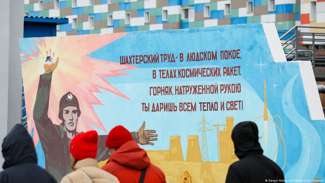 Люди рассматривают плакат, посвященный угольной промышленности, в российском шахтерском поселке Баренцбург на норвежском архипелаге Шпицберген.