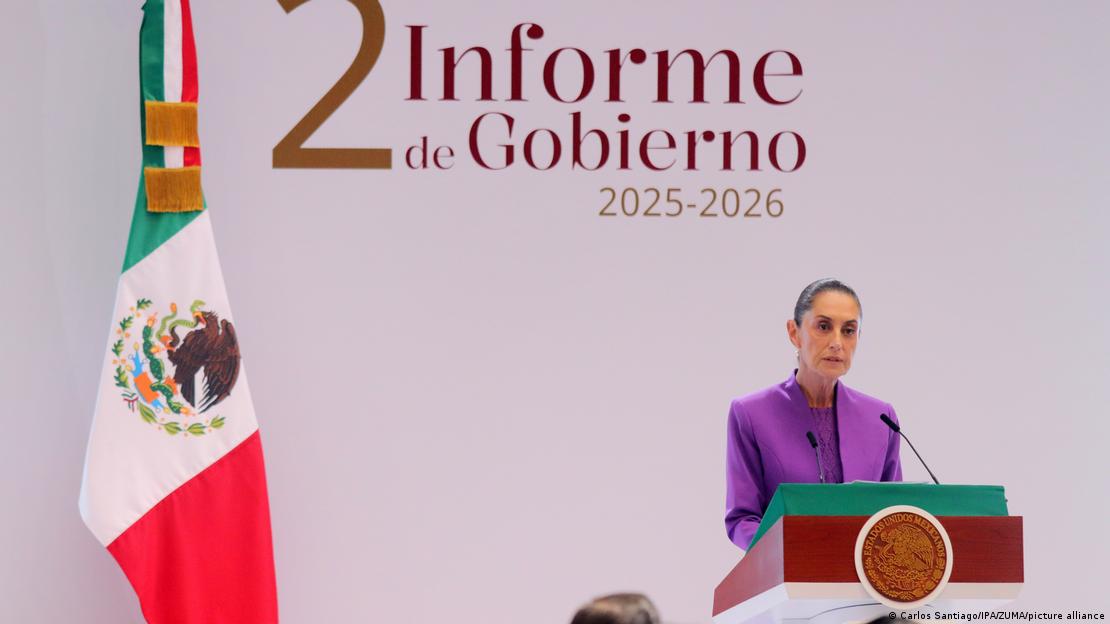  Claudia Sheinbaum en una conferencia de prensa oficial. La bandera de México junto a ella. Detrás, un letrero pone "2° informe de gobierno 2025-2026"