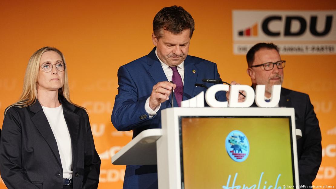 CDU'lu Saksonya Anhalt Başbakanı Sven Schulze seçim yenilgisinin ardından kürsüre açıklama yaparken. İki CDU'li siyasetçinin ortasında yüzünde üzgün bir ifade ile CDU'lu Saksonya Anhalt Başbakanı Sven Schulze seçim yenilgisinin ardından kürsüre açıklama yaparken. İki CDU'li siyasetçinin ortasında yüzünde üzgün bir ifade ile