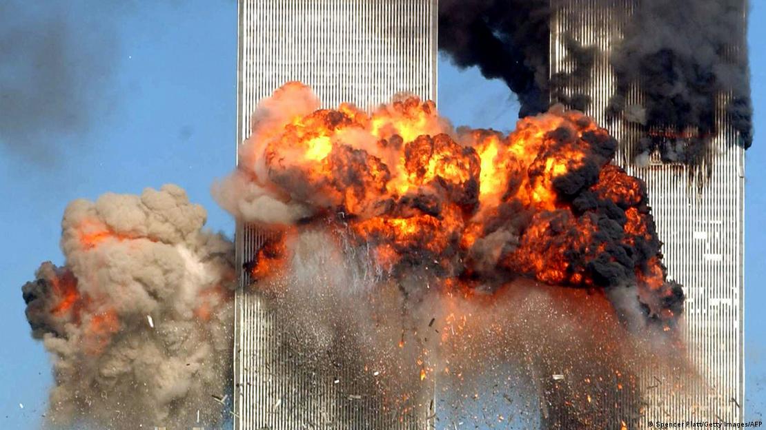 A glowing red fireball engulfs the left tower of the World Trade Center in New York. The upper section of the second tower is shrouded in thick black smoke.