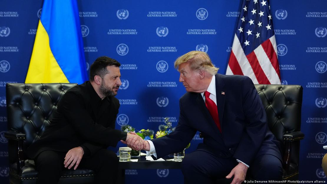 El presidente ucraniano estrecha la mano de su homólogo estadounidense con sus respectivas banderas detrás.