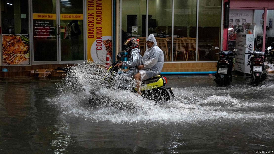 Commuters ride on a scooter through flood waters after heavy rain in Bangkok