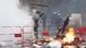 Manifestante lanza un madero sobre una barricad incendiada.