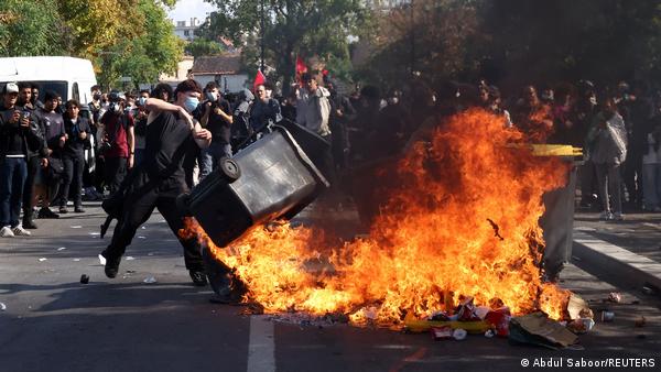 A masked protester throws a garbage bin into a fire set up by high school and university students in a street amid clashes with French riot police during a student protest
