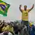 Flávio Bolsonaro acena para seguidores, um deles empunha a bandeira do Brasil