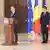 Un bărbat, premierul desemnat Luca Niculescu, vorbește la microfonul Președinție.În spatele lui, un alt bărbat, președintele Nicușor dan, în fața steagurilor României și UE, îi urmărește discursul.