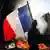 A protester waving a French national flag walks past a fire during clashes prior to the start of a demonstration to protest against the high cost of living