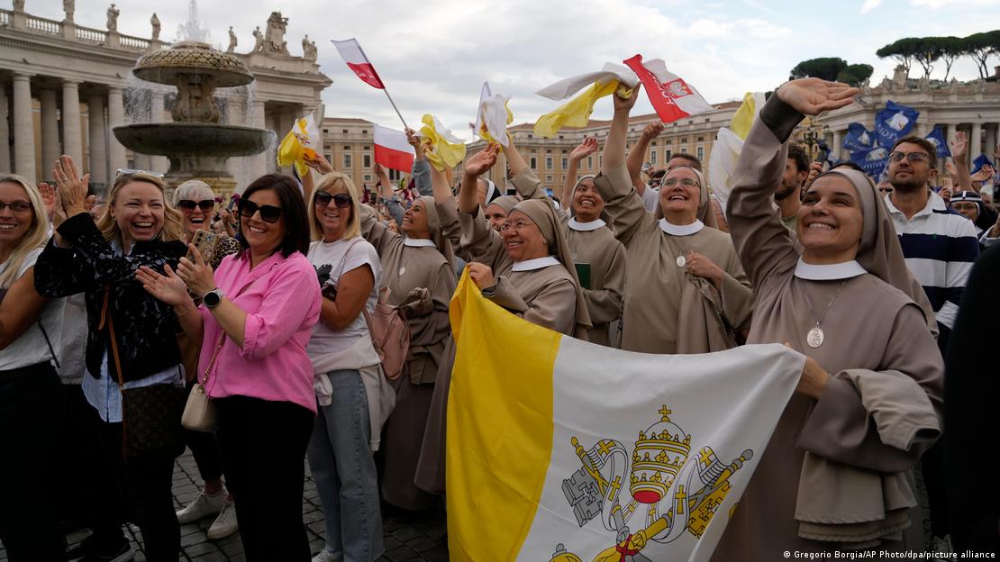 Un grupo de religiosas sostiene la bandera del Vaticano rodeadas por una multitud.