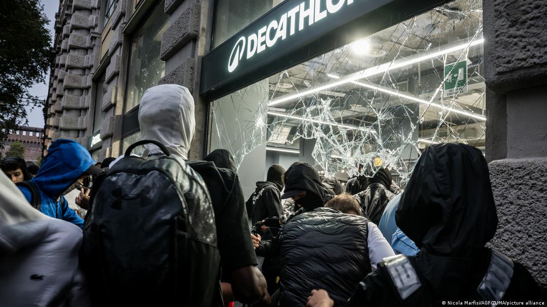 İtalya'nın Milano kentinde yüzleri maskeli protestocular bir mağazanın camını kırarken. 