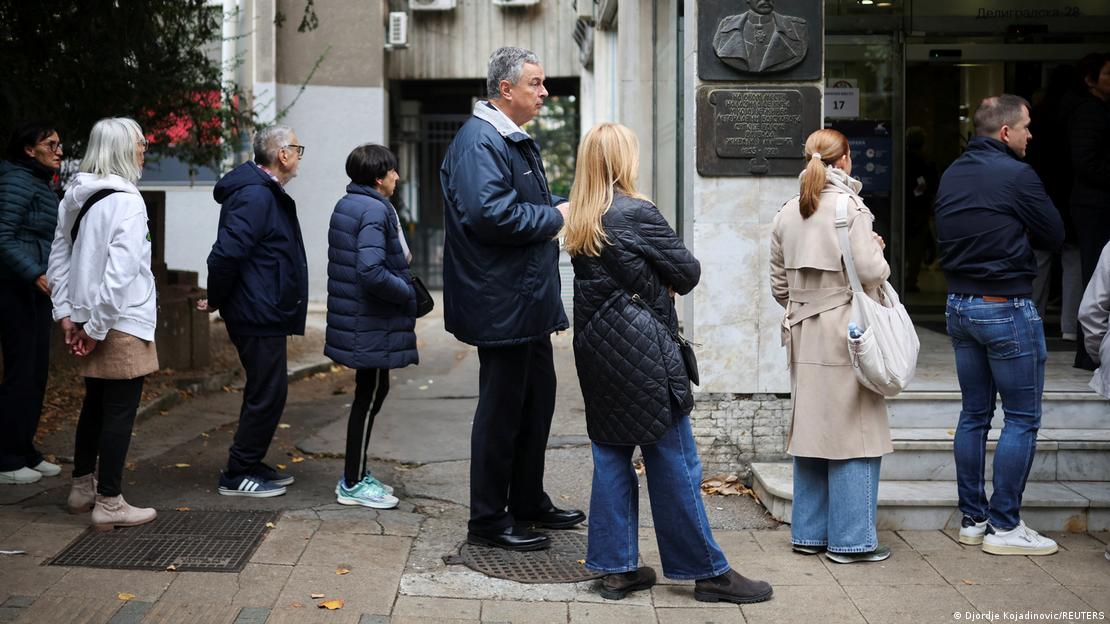 Menschen in einer Schlange vor einem Gebäude, in der Mitte ein größerer Mann (Dejan Soskic) Menschen in einer Schlange vor einem Gebäude, in der Mitte ein größerer Mann (Dejan Soskic)