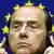 Italian Prime Minister Silvio Berlusconi adjusts his earphones with the EU flag behind him