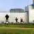 A father and his two children run on the grass outside a nuclear power plant